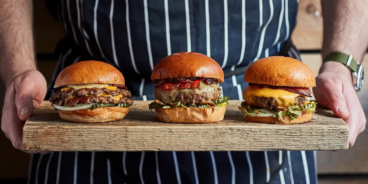 Ein Mitglied des Holy-Cow-Teams serviert drei Burger